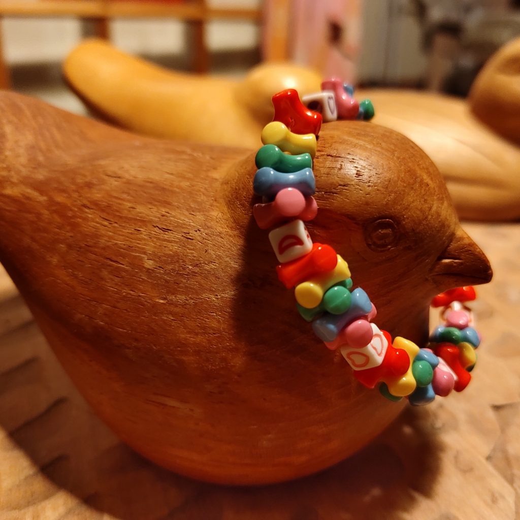 A carved wooden bird sits adorned with a colourful plastic children's bracelet.