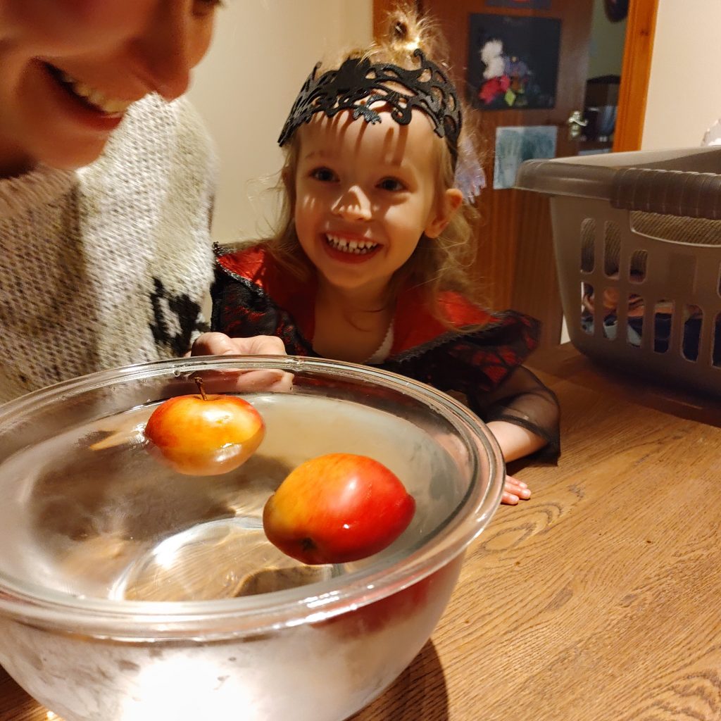A preschooler grins at a woman just about to participate in apple ducking (or bobbing).